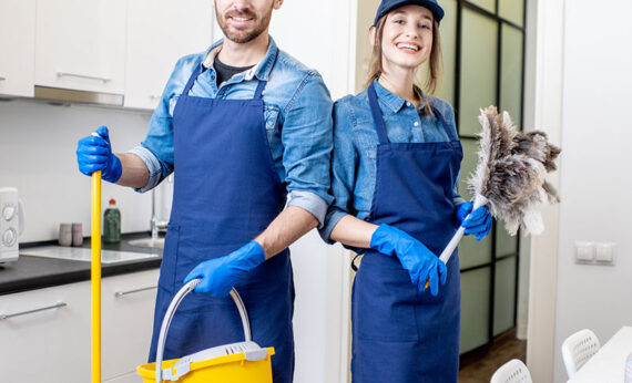 Portrait of a couple as a professional cleaners in uniform standing together with cleaning tools indoors